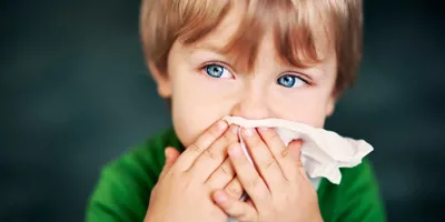 Un petit garçon est en train de se moucher. Il présente des symptômes de l’allergie à la poussière.