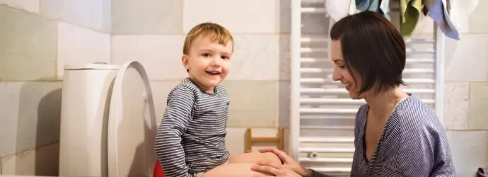 : Un enfant est sur les toilettes d’une salle de bain face à sa mère qui lui apprend la propreté.  
  
