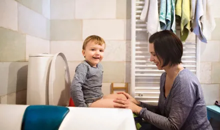 Un petit garçon souriant assis sur des toilettes accompagné de sa mère