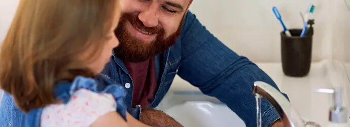 Un père sourit à sa petite fille en lui apprenant les règles d’hygiène de base comme se laver les mains. 