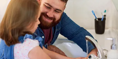 Un père sourit à sa petite fille en lui apprenant les règles d’hygiène de base comme se laver les mains. 