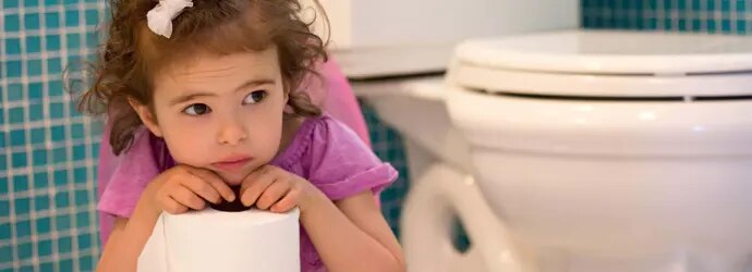 Une fille assise sur un pot se penche en avant tout en gardant un rouleau de papier toilette.