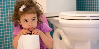 Une fille assise sur un pot se penche en avant tout en gardant un rouleau de papier toilette.