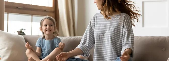 Femme et enfant assis en position de méditation sur un canapé.