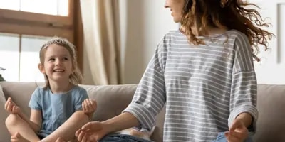 Femme et enfant assis en position de méditation sur un canapé.