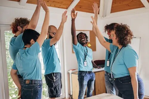 Six personnes, toutes vêtues de t-shirts bleus, rient et se congratulent dans un groupe.