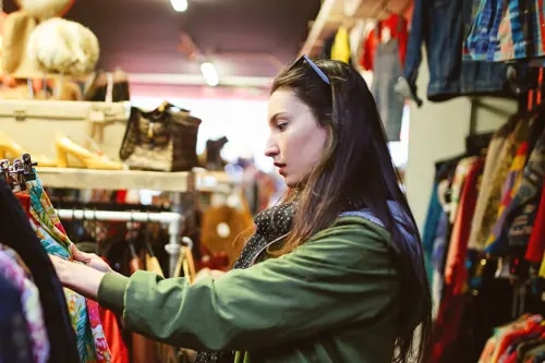 Une femme fait ses courses seule dans un magasin de charité, inspectant des rails de vêtements.