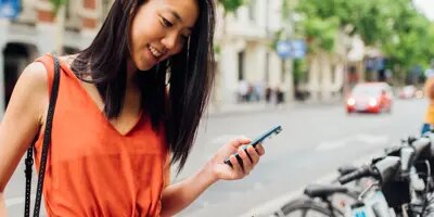 Une jeune femme consulte son téléphone près d'une station de vélos en libre-service.