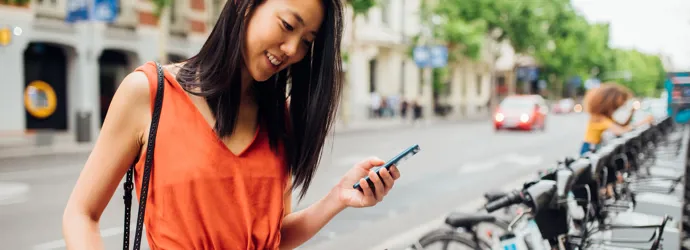 Une jeune femme consulte son téléphone près d'une station de vélos en libre-service.