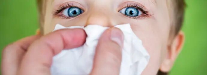 Enfant qui se fait couvrir le nez d'un mouchoir.