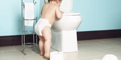 Bébé qui regarde dans les toilettes. Un dérouleur de papier toilette est à côté de lui. 