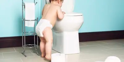 Bébé qui regarde dans les toilettes. Un dérouleur de papier toilette est à côté de lui.