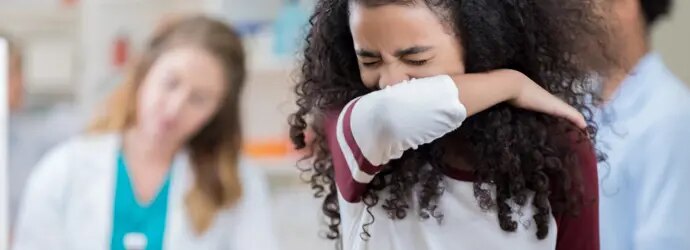 Une enfant est en train d’éternuer dans son coude pour ne pas transmettre les microbes.  