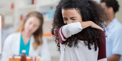Une enfant est en train d’éternuer dans son coude pour ne pas transmettre les microbes.