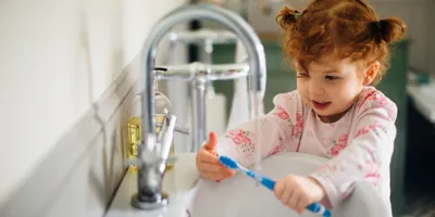 Une petite fille rousse lave sa brosse à dents dans un lavabo