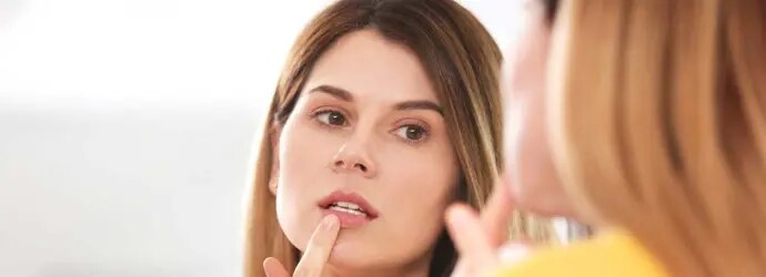 Femme traite un bouton de fièvre devant le miroir