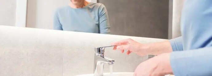 Une femme âgée utilise le robinet  pour nettoyer sa brosse à dents