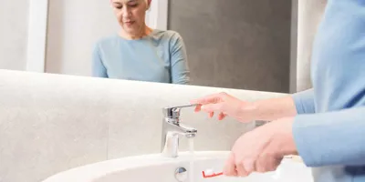 Une femme âgée utilise le robinet  pour nettoyer sa brosse à dents
