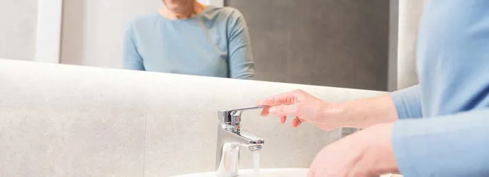 Une femme âgée utilise le robinet  pour nettoyer sa brosse à dents