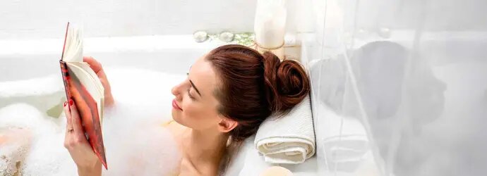 Une femme lit dans un bain à bulles avec des bougies allumées