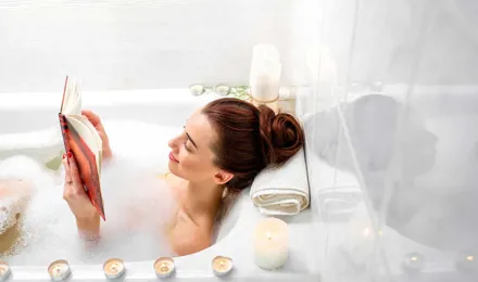 Une femme lit dans un bain à bulles avec des bougies allumées