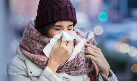Paksuihin talvivaatteisiin sonnustautunut nainen kärsii poskiontelotulehduksen oireista ja aivastaa nenäliinaan ulkona