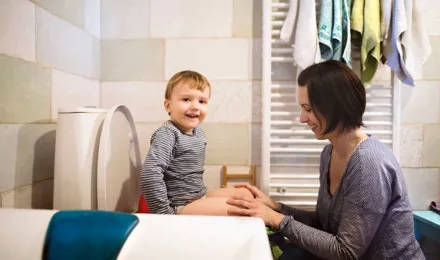Äiti auttaa poikaansa istumaan vessassa potalla