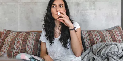 Une jeune femme avec une allergie au pollen de bouleau est assise sur le canapé et porte un spray nasal à son nez