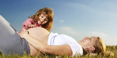 Une mère enceinte et son jeune enfant assis dans un champ avec un ciel bleu semble avoir besoin de soulager son rhume des foins pendant la grossesse.