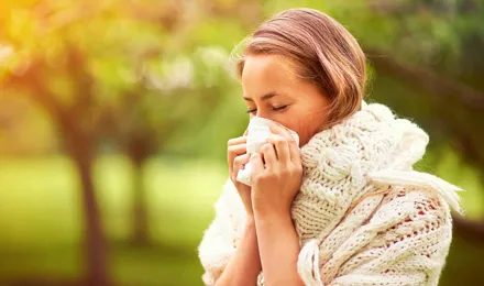 Une jeune femme éternue dans un parc et s'interroge sur les causes du rhume des foins