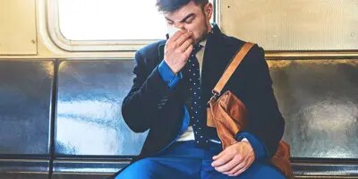 Un homme vêtu d'un costume se mouche assis dans un wagon de train