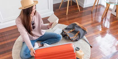 Une jeune femme assise sur le plancher prépare sa valise pour les vacances d'été