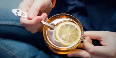 Deux mains tiennent une tasse de thé avec du citron, excellent remède contre le nez qui coule.