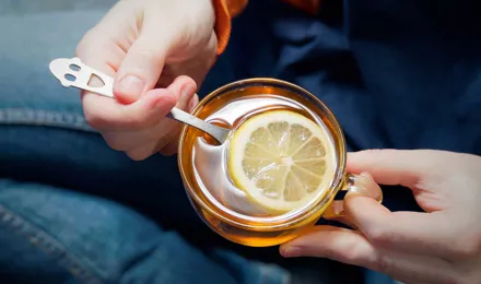 Deux mains tiennent une tasse de thé avec du citron, excellent remède contre le nez qui coule.