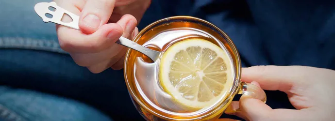 Une personne tient une tasse en verre remplie d'eau chaude avec du miel et du citron