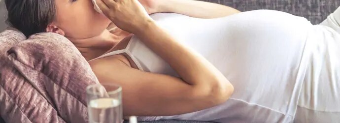 Une jeune femme enceinte avec un rhume sur le canapé.