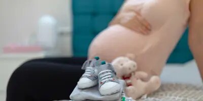 Un tas soigné de vêtements de bébé sur un lit avec une femme enceinte assise en arrière-plan
