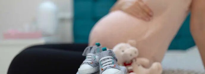 Un tas soigné de vêtements de bébé sur un lit avec une femme enceinte assise en arrière-plan