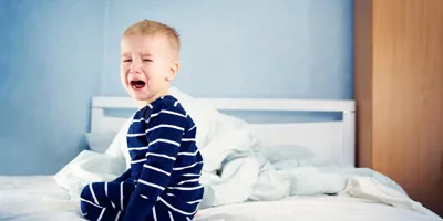 Un jeune enfant pleure assis sur un lit 
