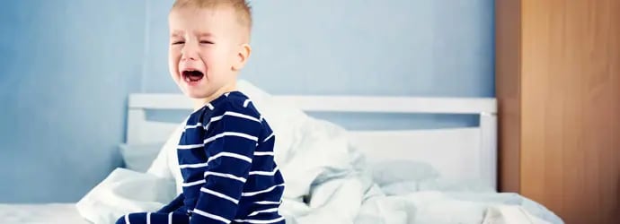 Un jeune enfant pleure assis sur un lit
