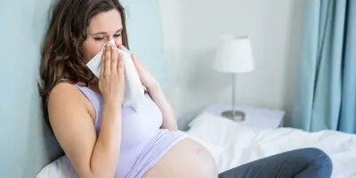 Une femme enceinte assise sur un lit se mouche dans un mouchoir