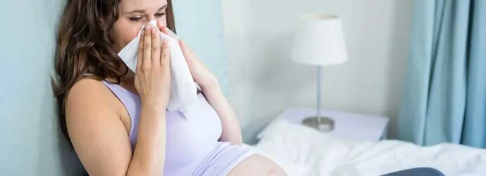 Une femme enceinte assise sur un lit se mouche dans un mouchoir