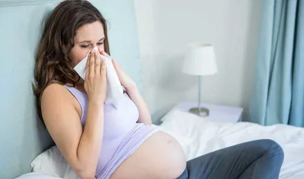 Une femme enceinte assise sur un lit se mouche dans un mouchoir