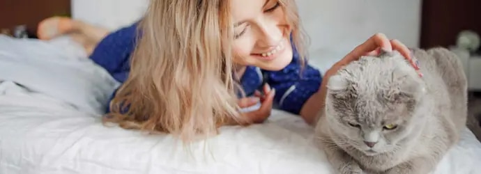 Nainen makaa sängyllä ja silittää kissaansa allergiaoireista kärsimättä