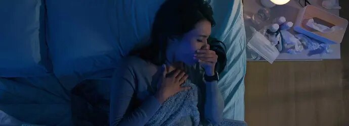 Une femme dans son lit souffre de toux la nuit, à côté d’elle se trouvent des mouchoirs usagés et des médicaments.