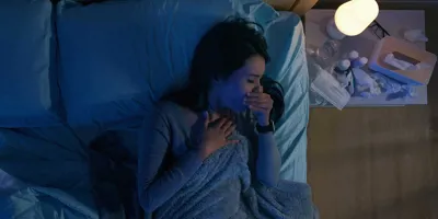 Une femme dans son lit souffre de toux la nuit, à côté d’elle se trouvent des mouchoirs usagés et des médicaments.