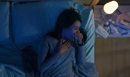 Une femme dans son lit souffre de toux la nuit, à côté d’elle se trouvent des mouchoirs usagés et des médicaments.