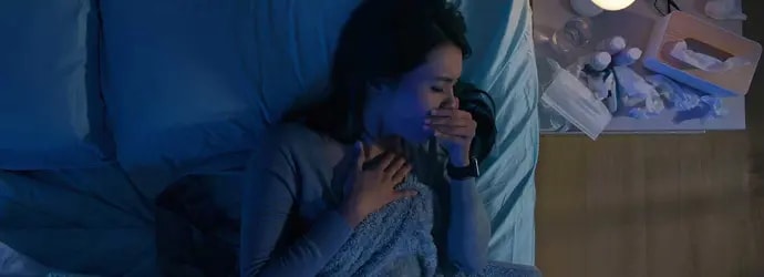Une femme dans son lit souffre de toux la nuit, à côté d’elle se trouvent des mouchoirs usagés et des médicaments.