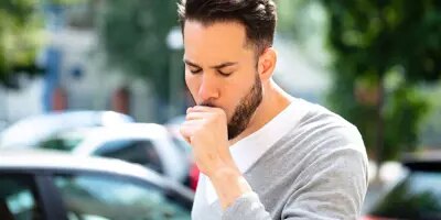 Un homme tousse, il est entouré de voitures