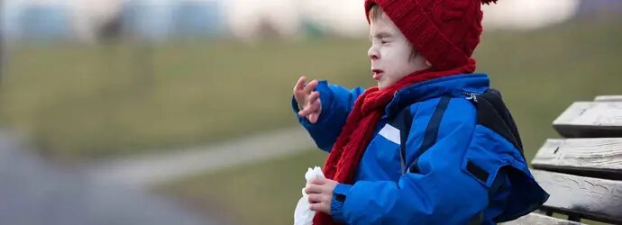 Une enfant éternue sur un banc dans un parc en hiver